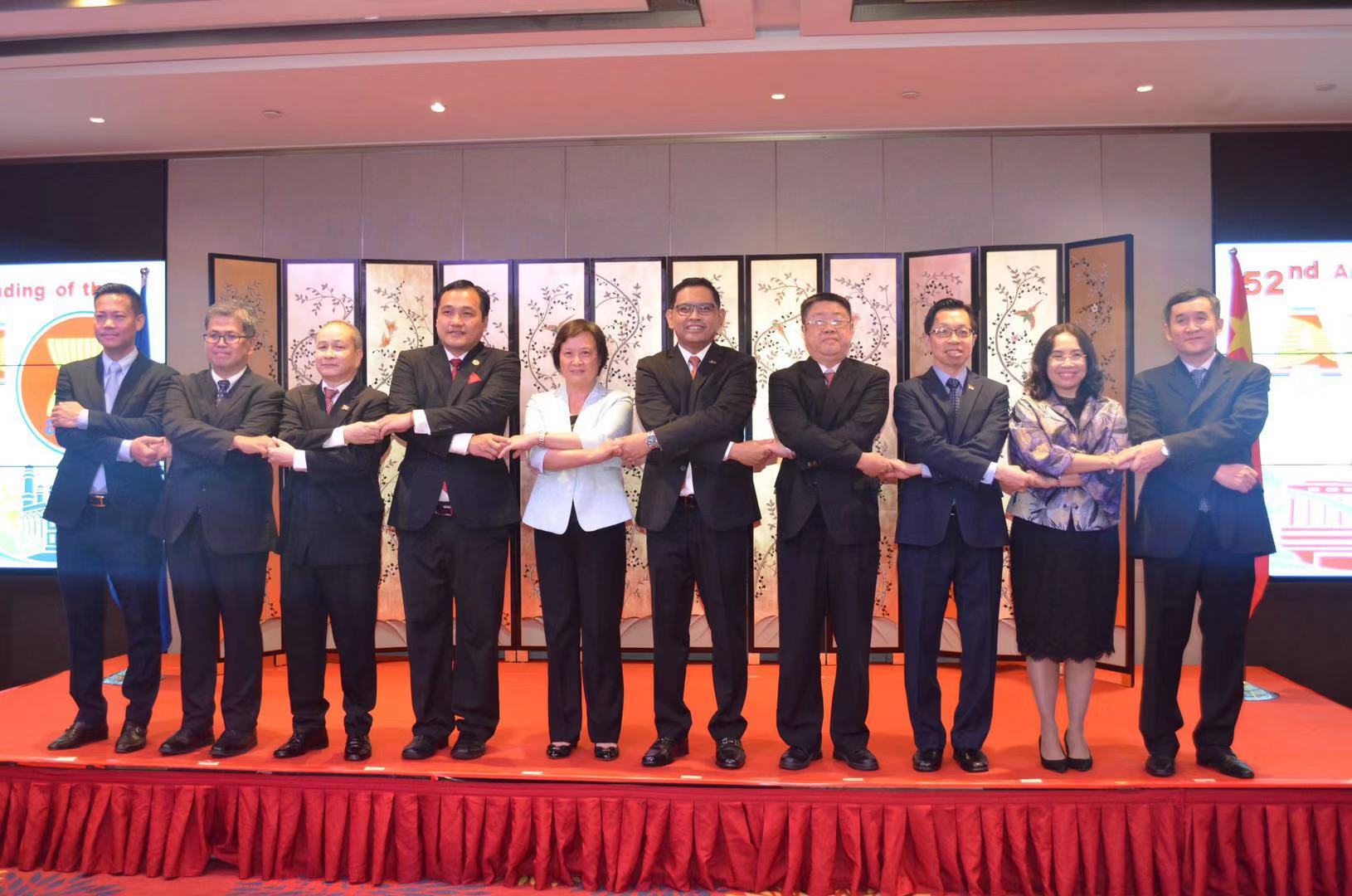 Group of ten people in suits holding hands in a line on a red platform, stage backdrop behind.